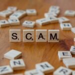 Scrabble tiles spelling the word SCAM on a wooden table, illustrating a guide to spotting phishing and scam messages