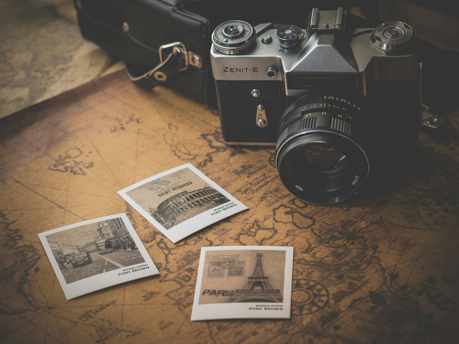 DSLR camera beside scattered printed photographs on a vintage map, illustrating how to organize a digital photo library